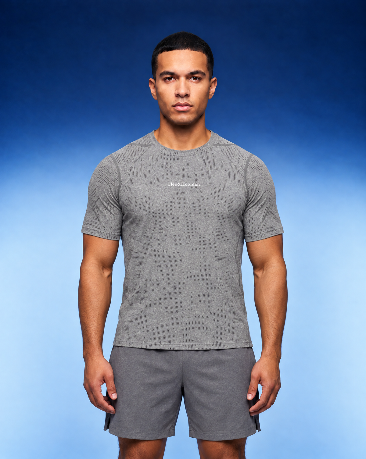 A man modeling a gray short-sleeve athletic t-shirt with a subtle textured pattern and a small white 'Check Runners' logo on the chest, paired with matching gray shorts, set against a blue gradient studio background.
