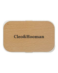 A rectangular compact case with rounded corners, featuring a light natural wood grain top and a white border, with the brand name 'Cleo&Hooman' printed in black serif text in the center.
