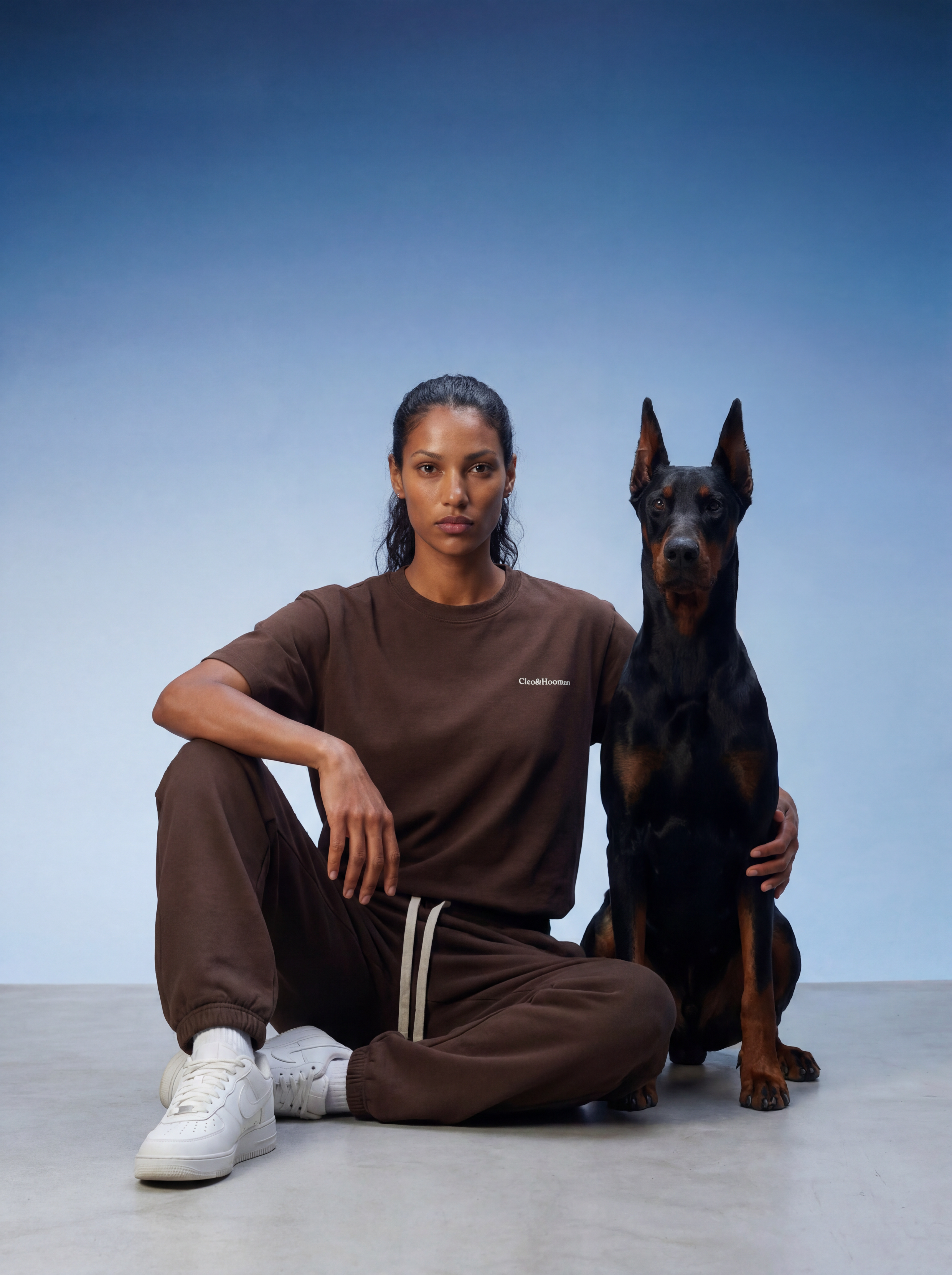 Person wearing a brown outfit sitting next to a black dog on a light blue background