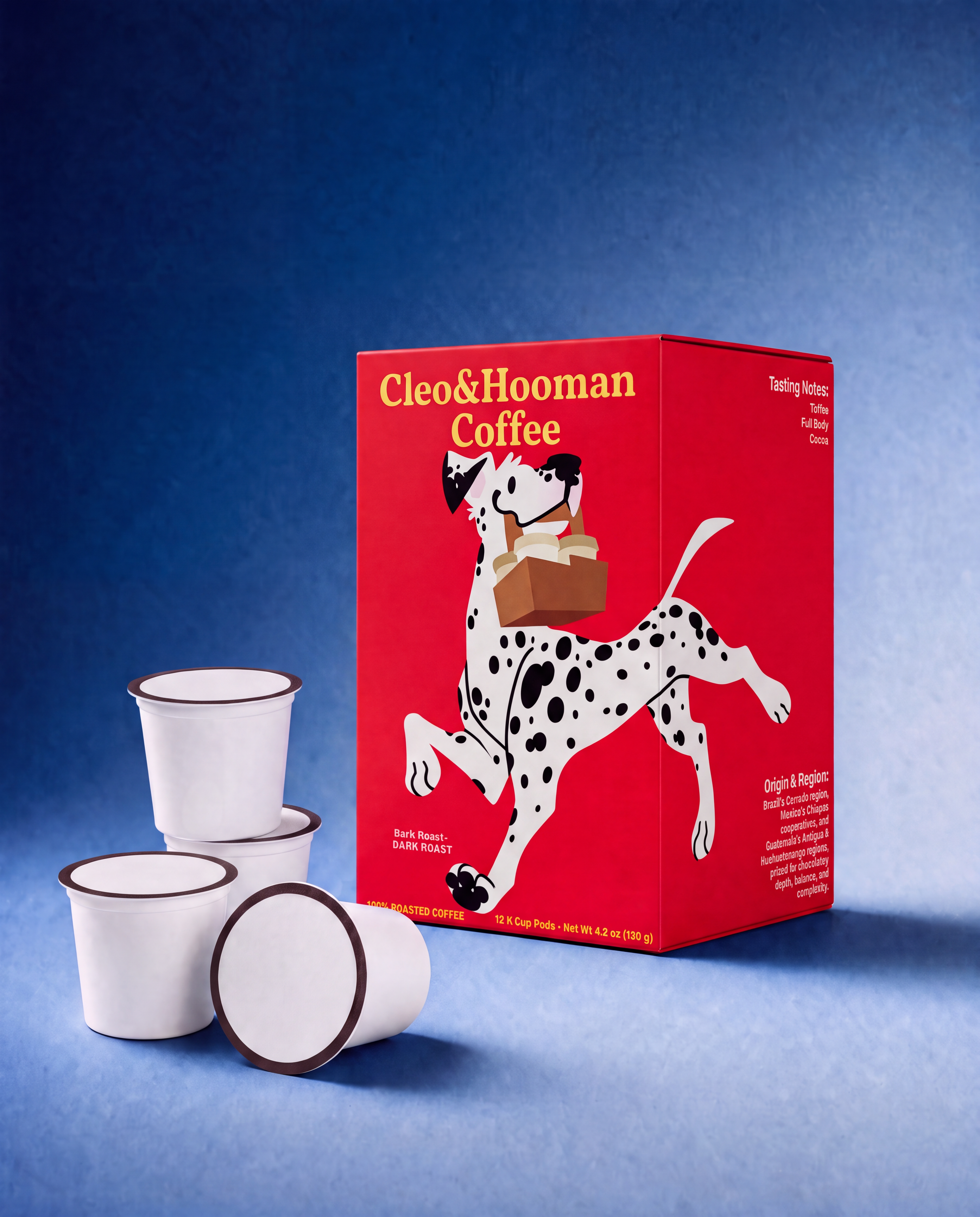 A red Cleo & Hooman Coffee box with a Dalmatian illustration stands on a blue studio background, with three white coffee pods arranged in front.