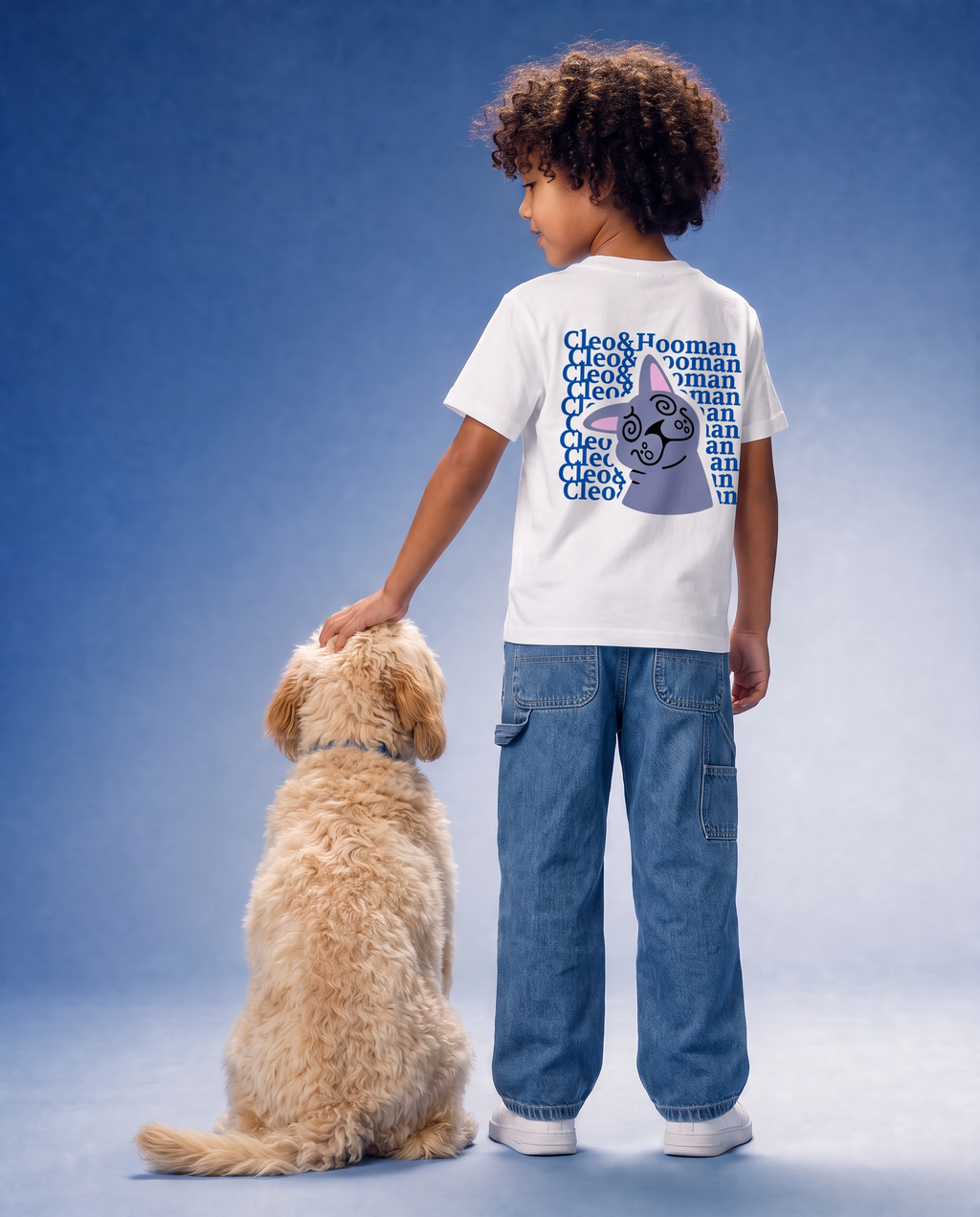 A child wearing a white graphic T-shirt and blue jeans stands with a golden dog against a blue studio background. The child is shown from the back, and the shirt features a large blue and purple Cleo deities graphic.