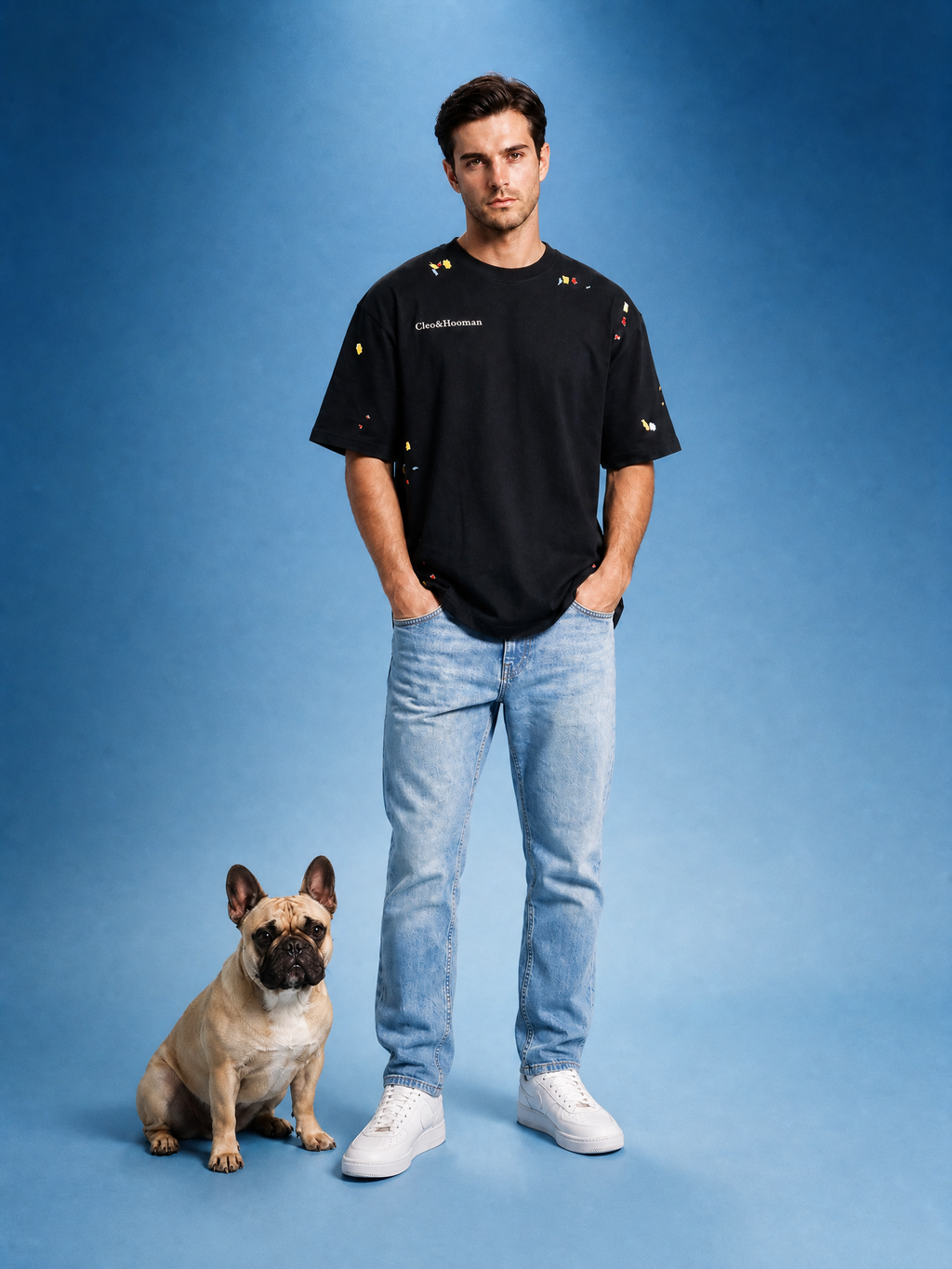 Man wearing a black t-shirt and blue jeans standing next to a dog on a blue background