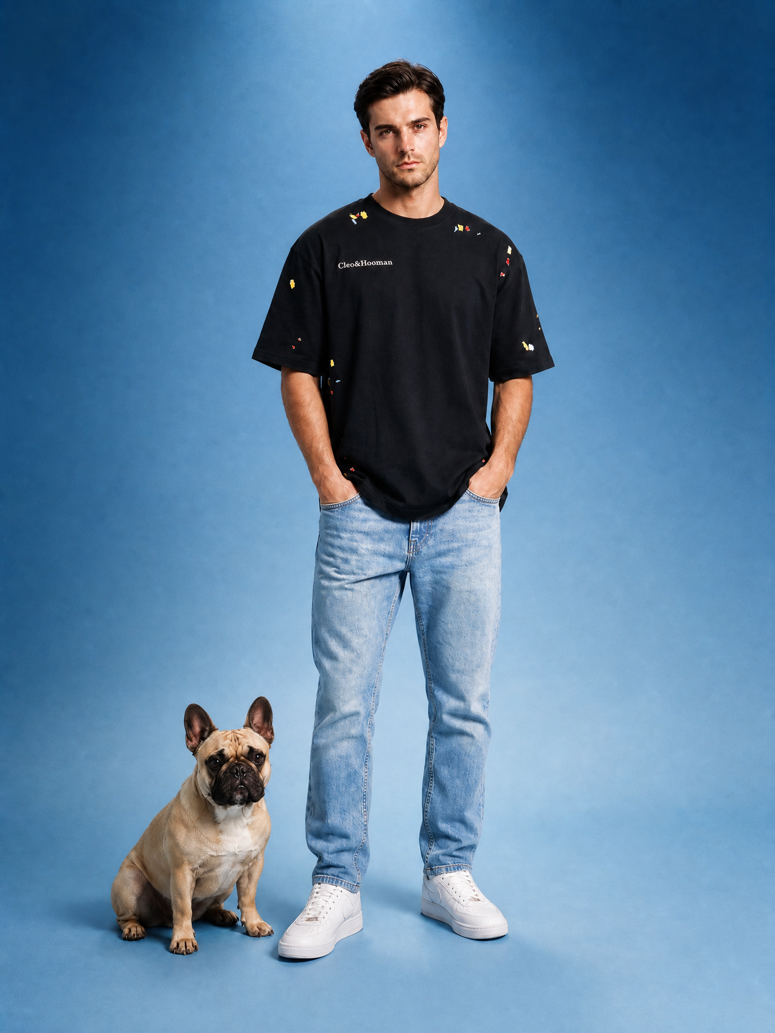 Man wearing a black t-shirt and blue jeans standing next to a dog on a blue background