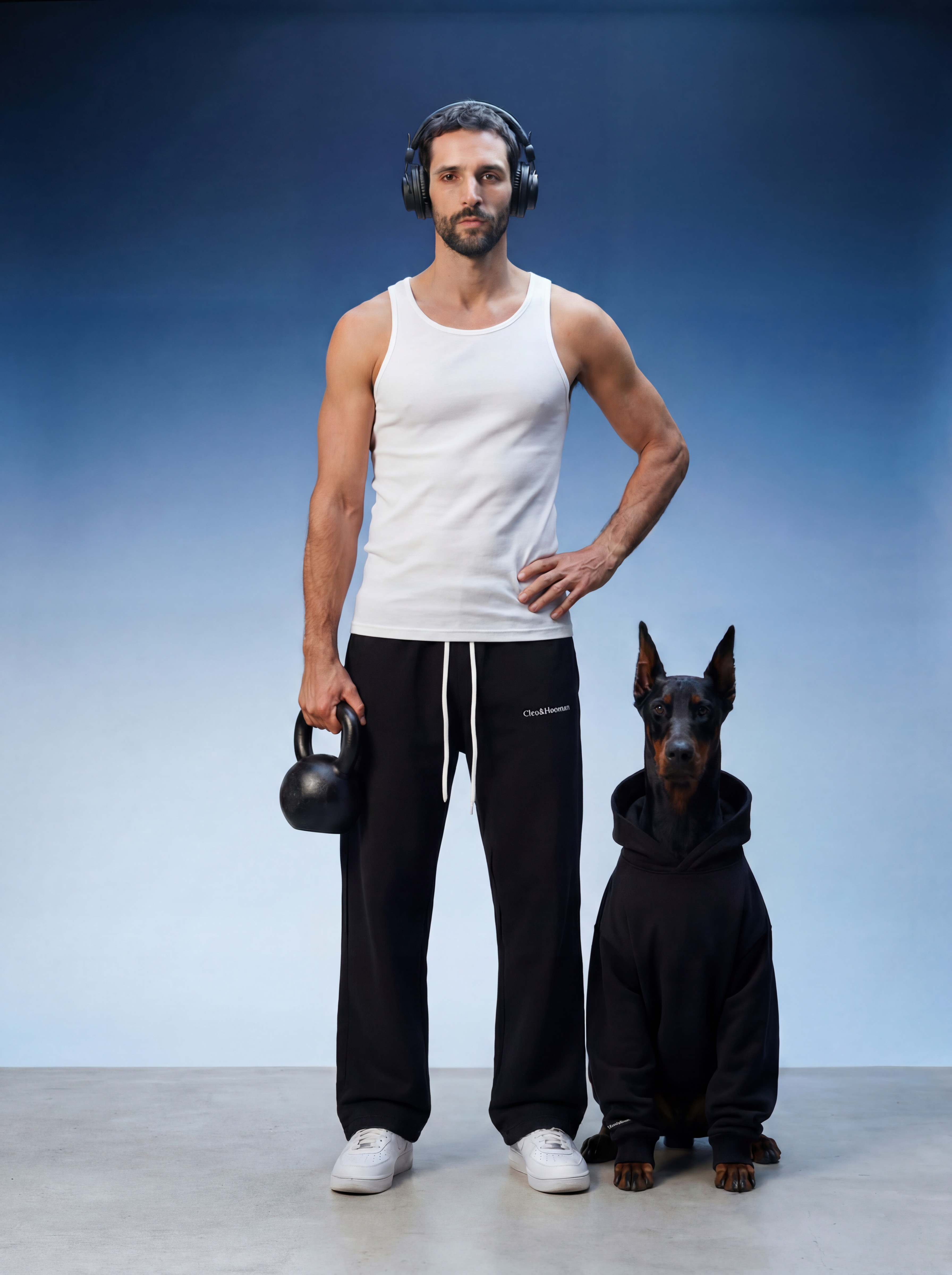 Man in white tank top and black pants holding a kettlebell, standing next to a dog in a black outfit on a blue background