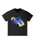 A black short-sleeve crewneck t-shirt featuring a cartoon graphic of a blue instant camera taking a photo, with a yellow sunburst and a printed photo coming out. The neck label shows the brand 'Cleo & Human'.